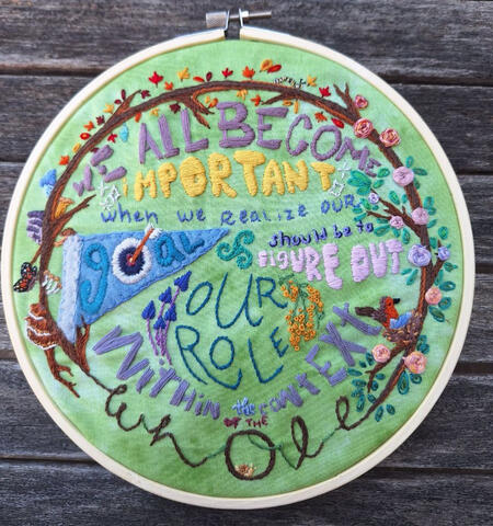 Hand-embroidered hoop art featuring the quote "We all become important when we realize our goal should be to figure out our role within the context of the whole" from the song I Like Giants by Kimya Dawson, with a life cycle theme.