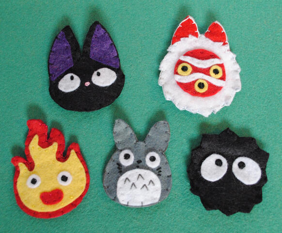 Hand-stitched felt set of hair clips featuring characters from Studio Ghibli movies: Jiji from Kiki's Delivery Service, Princess Mononoke's mask, Calcifer from Howl's Moving Castle, Totoro, and a Soot Sprite.